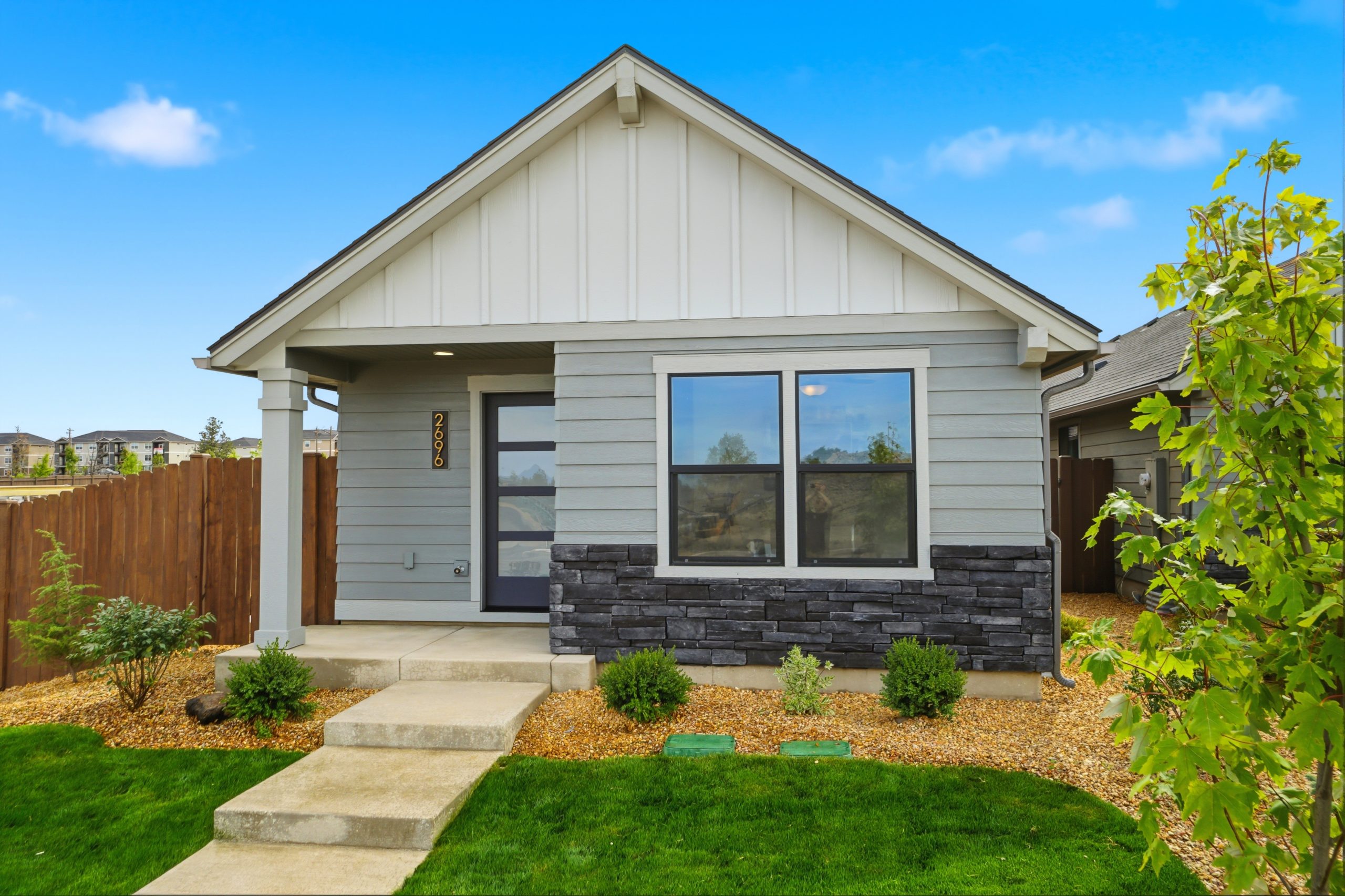 Exterior of a new Hayden Homes townhome at Hearthstone at Redmond Ranch in NW Redmond, Oregon, featuring masonry accents, black windows, and a covered front porch